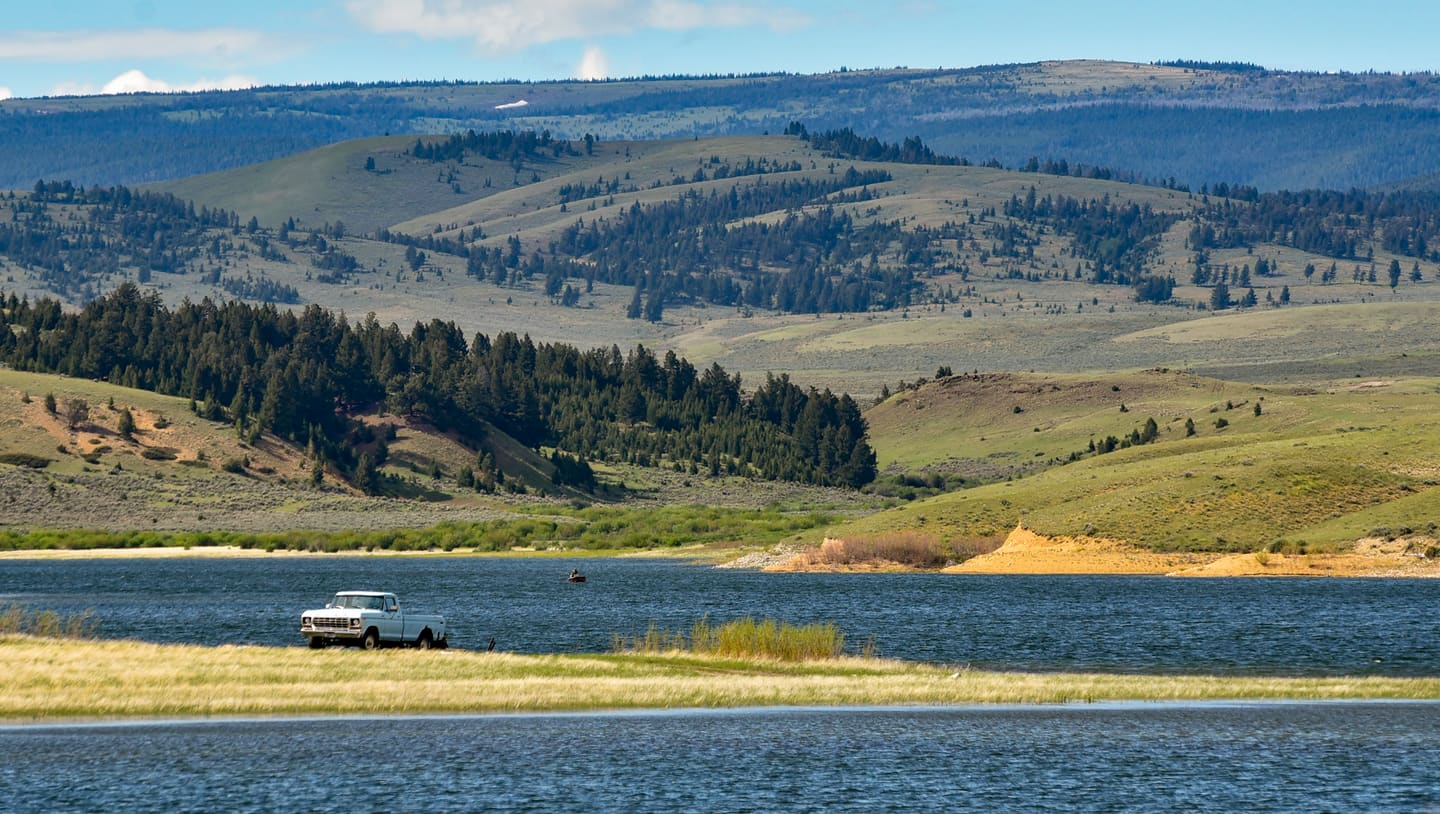 A pickup at the shore of Bair Reservoir below rolling timbered hills